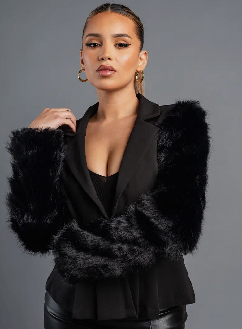 Woman wearing a black blazer with fur trim against a gray background