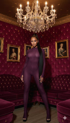Woman in a purple outfit standing in an opulent room with a chandelier and velvet furniture.