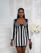 Woman wearing a black and white striped dress with long sleeves in a room with white walls and decor.