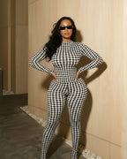 Person wearing a black and white checkered outfit standing against a beige wall.