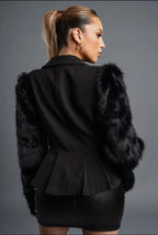 Black peplum jacket with fur trim worn by a person on a gray background