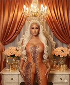 Woman in an orange patterned outfit standing in a luxurious room with orange curtains and chandelier.