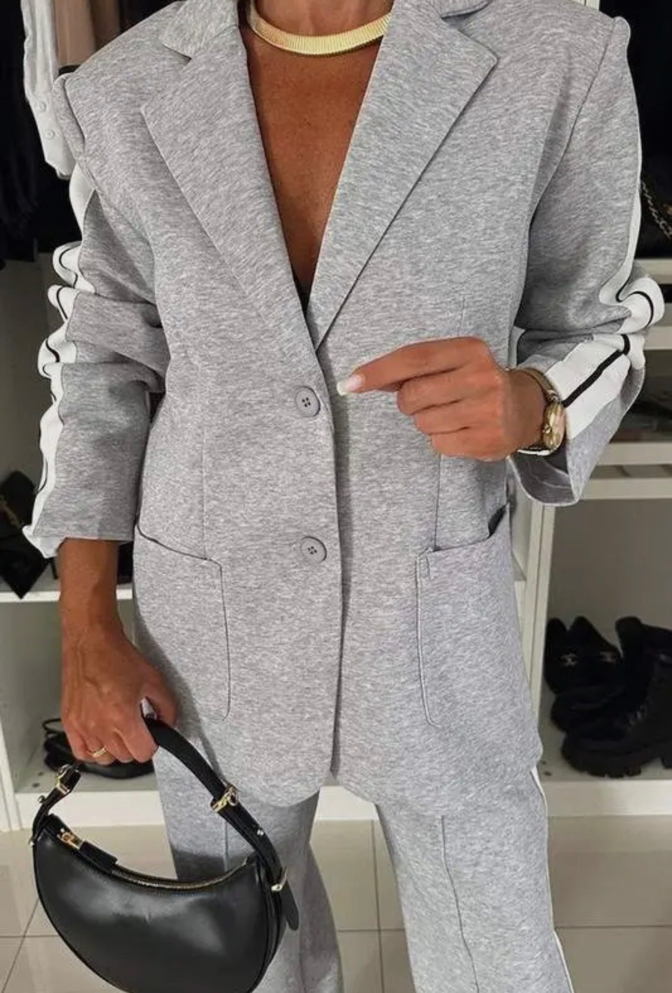 Person wearing a gray coat holding a black handbag indoors.