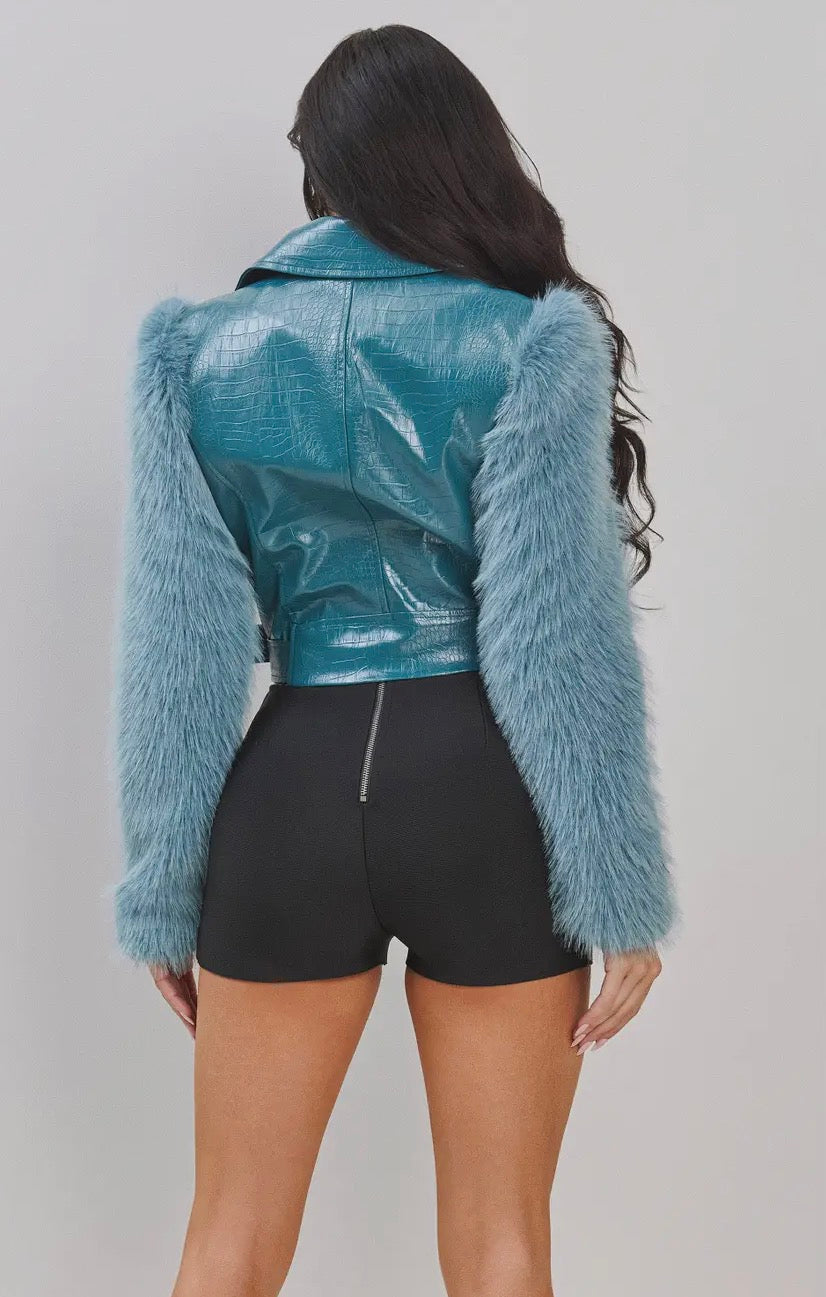 Person wearing a blue leather jacket with fur sleeves on a plain background