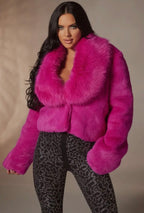 Woman wearing a bright pink fur coat against a neutral background