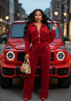 Woman in a red outfit standing in front of a red car on a city street.