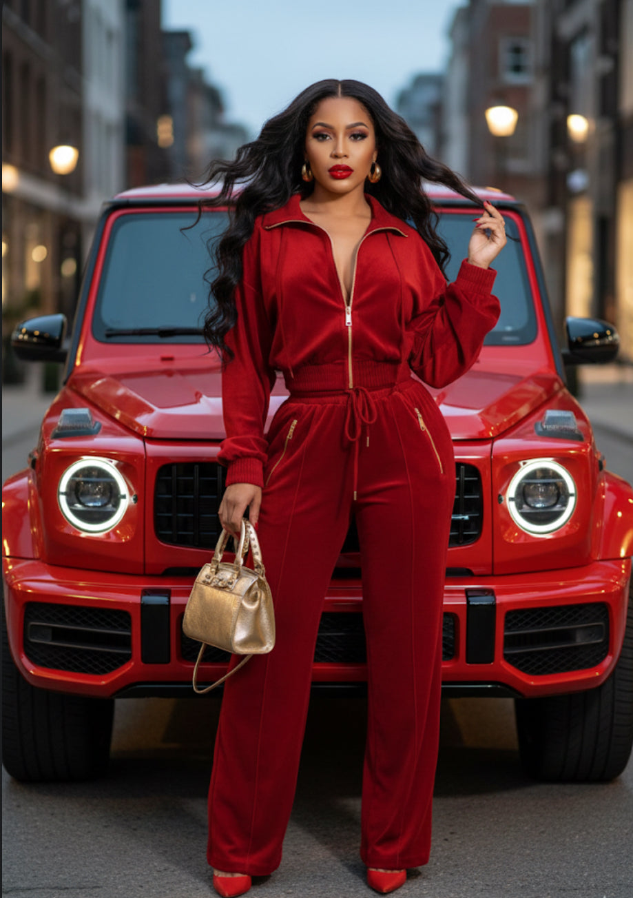 Woman in a red outfit standing in front of a red car on a city street.