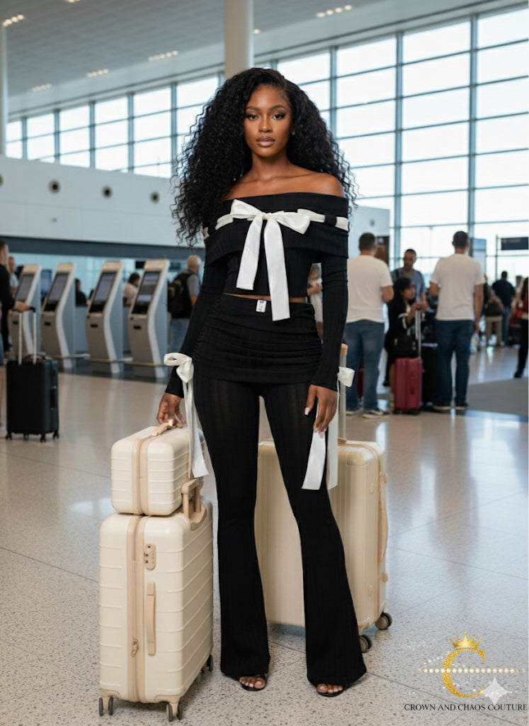 Woman in a black outfit with a white bow standing in an airport with luggage.