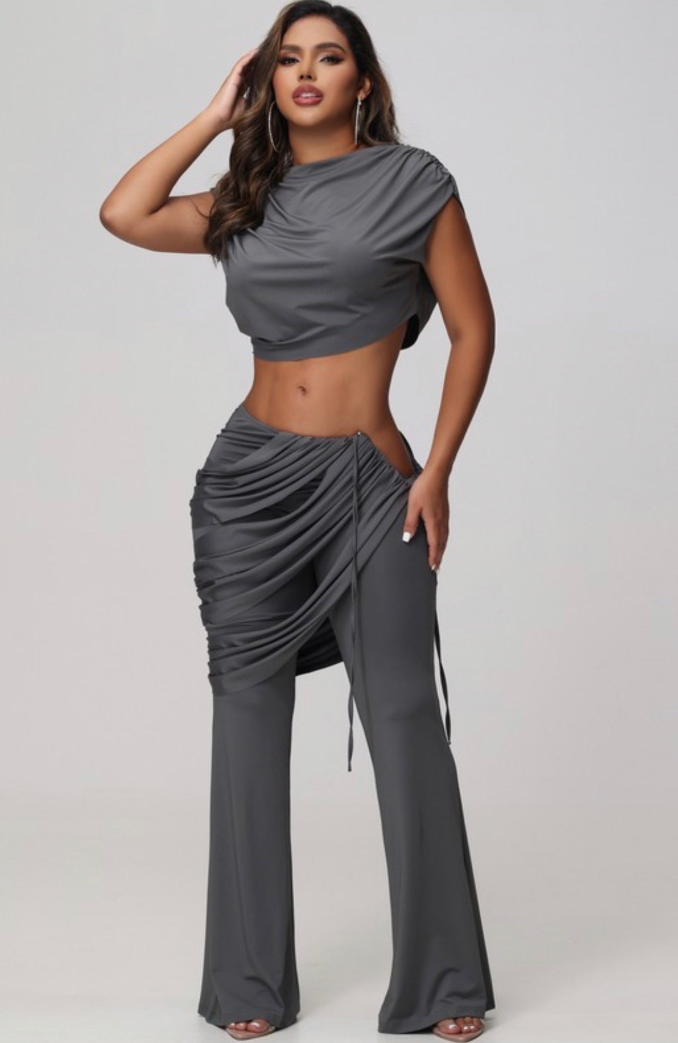 Woman wearing a gray outfit with draped design on a plain background