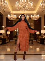 Woman in a rust-colored cable knit dress with a high slit standing in a luxurious room with chandeliers.