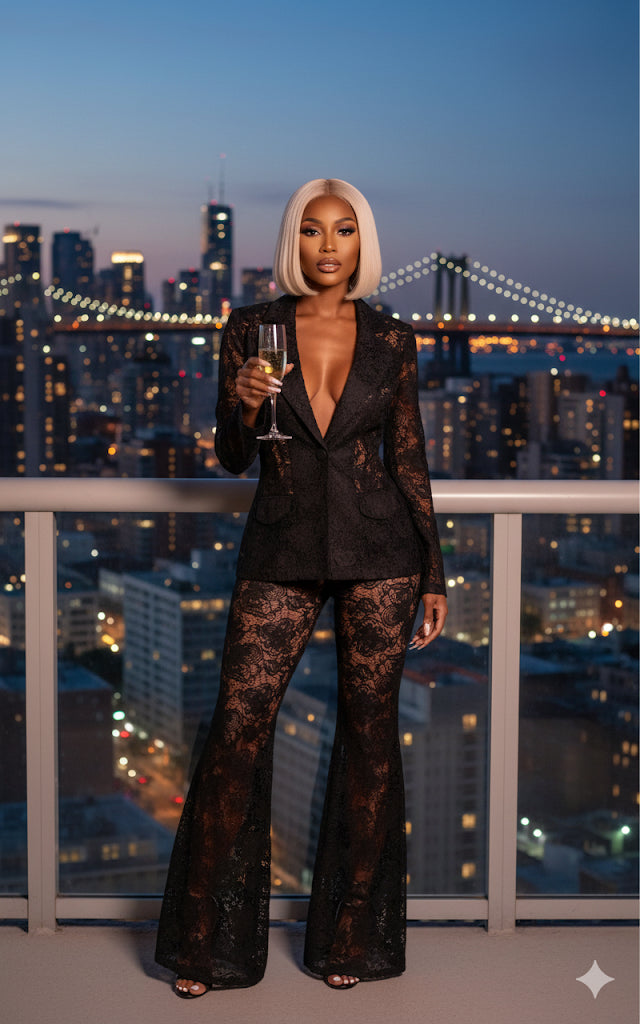 Woman in a black outfit with lace details holding a glass of wine on a balcony with city skyline view.