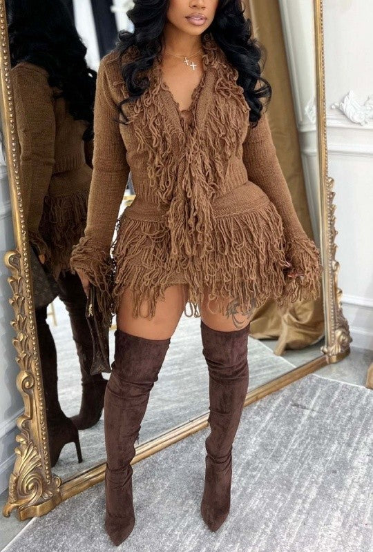 Woman wearing a brown fringed dress and knee-high boots in front of a mirror.