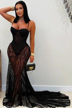 Woman wearing a black lace dress holding a handbag with a brand logo.