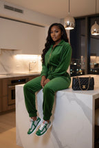 Woman in a green tracksuit sitting on a kitchen counter with a black handbag beside her.